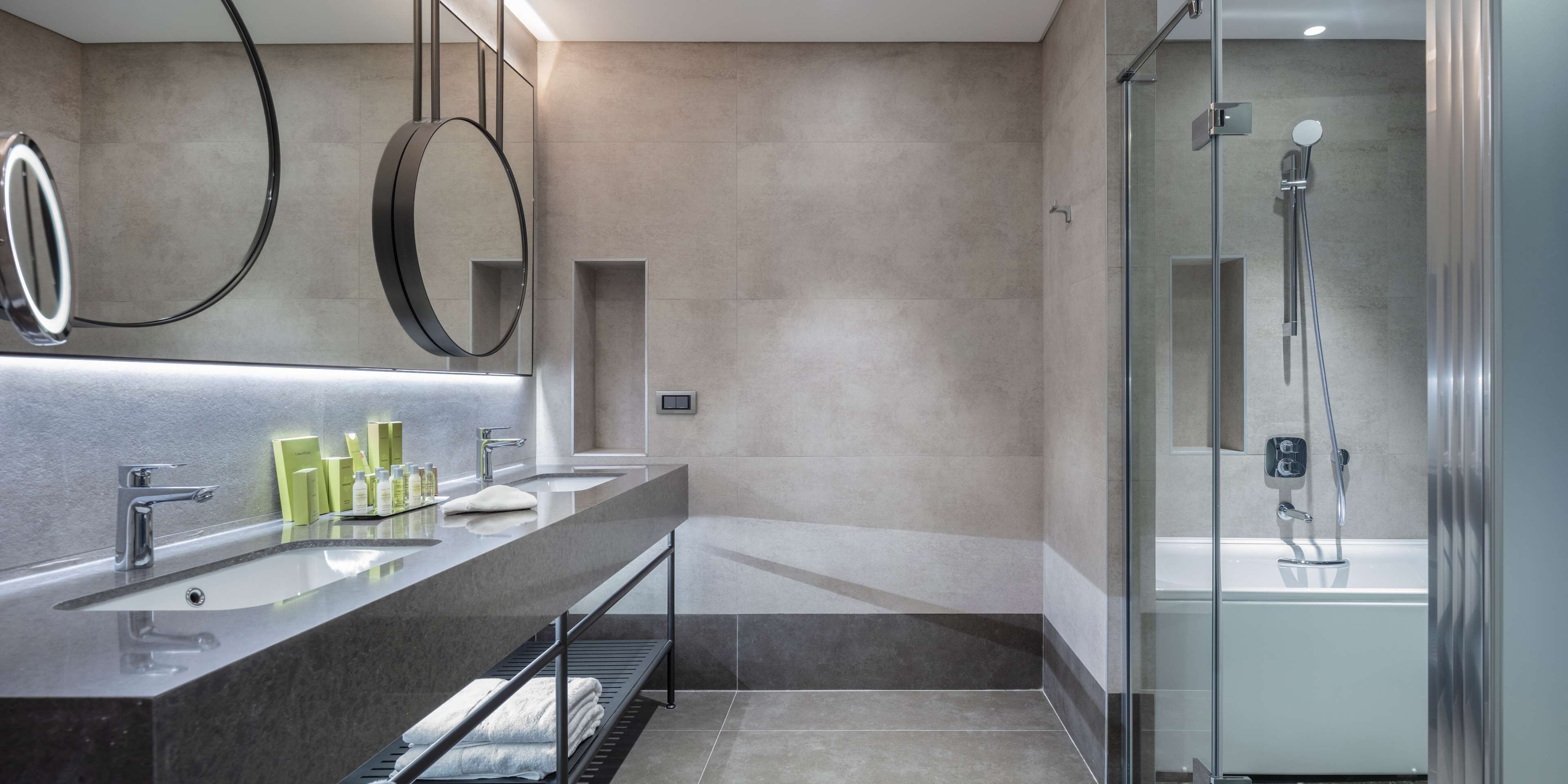 Un baño moderno con tocador doble lavamanos, un espejo grande y cabina de ducha con paredes de vidrio.