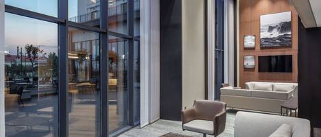 A modern lobby with large glass doors, a sofa, armchairs, and a coffee table.