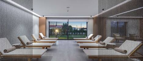 Un spa moderno con un ventanal grande que ofrece vistas a un puerto deportivo y árboles. Seis sillones de descanso están dispuestos en dos filas.