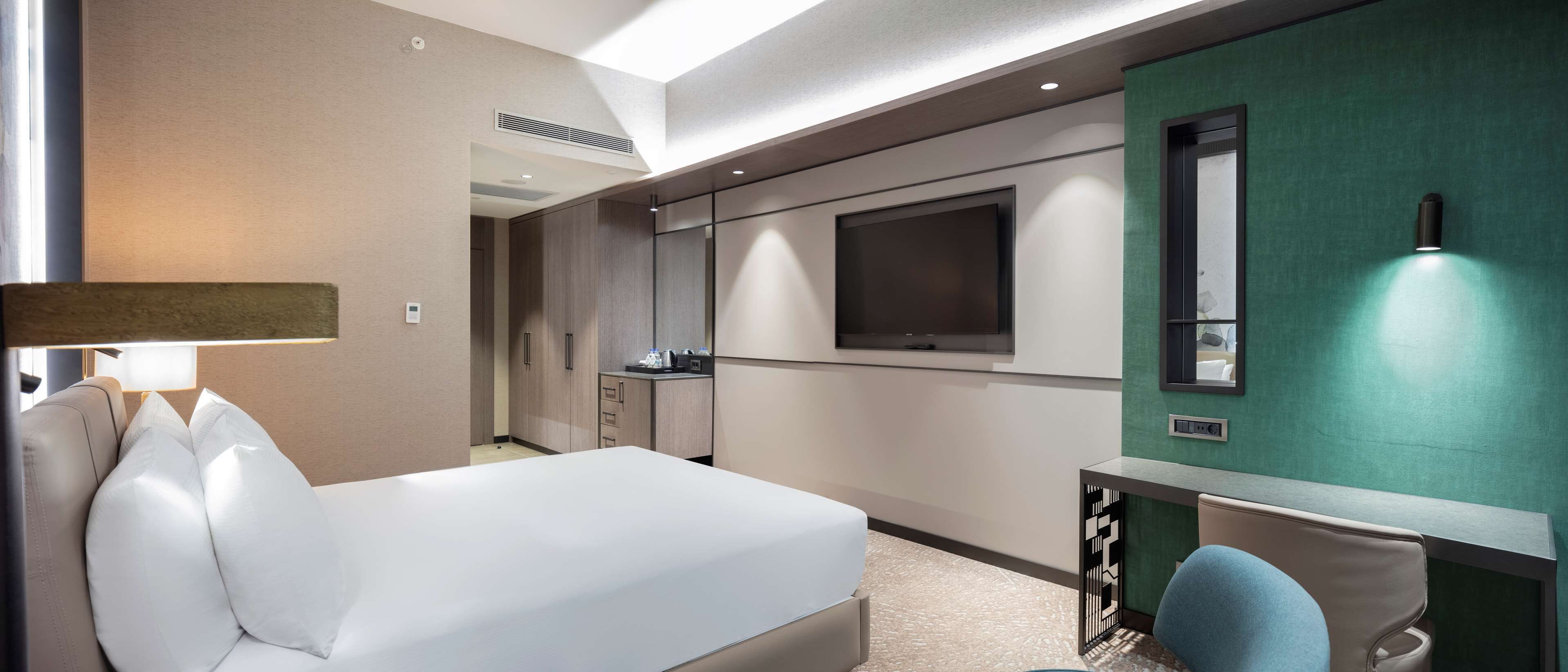 A hotel room with a bed, a desk, a chair, a TV, and a lamp.