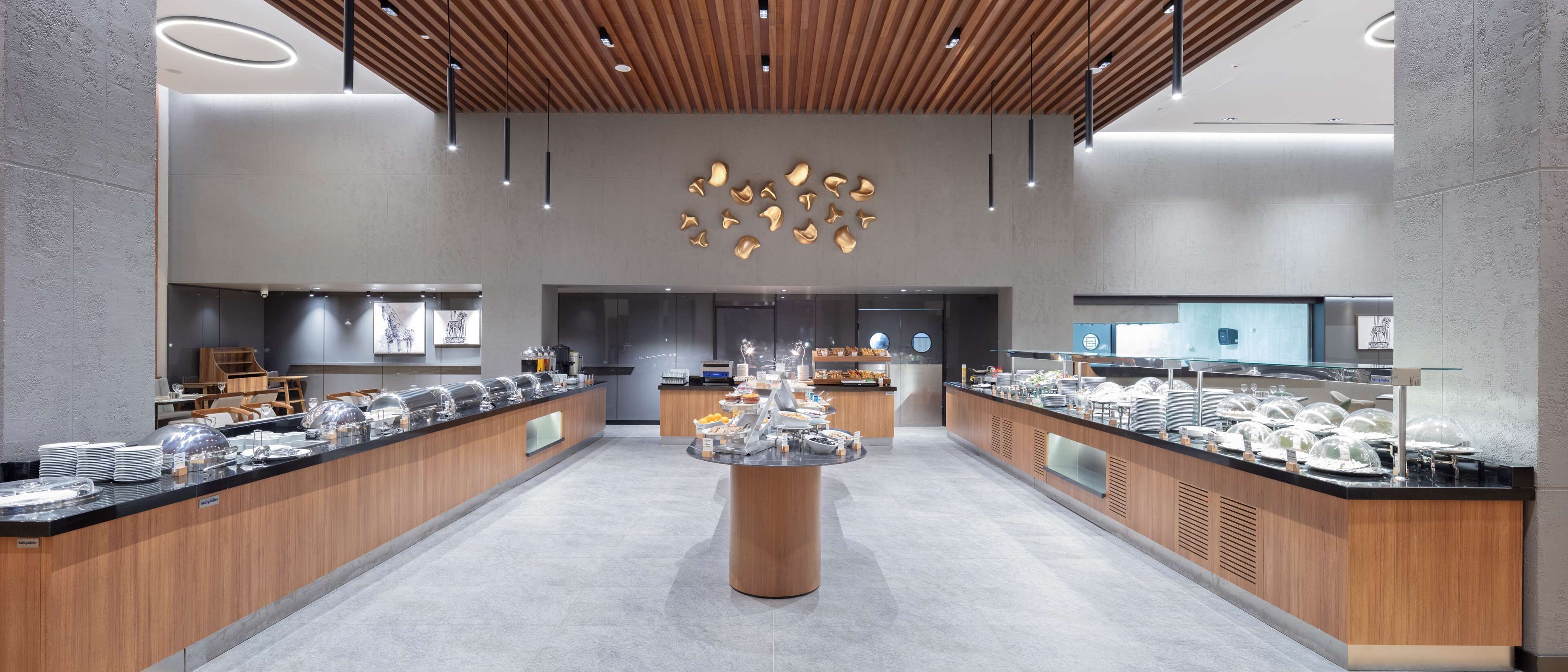 A modern buffet setup with a central serving area, multiple food stations, and a contemporary design with wooden accents and pendant lighting.