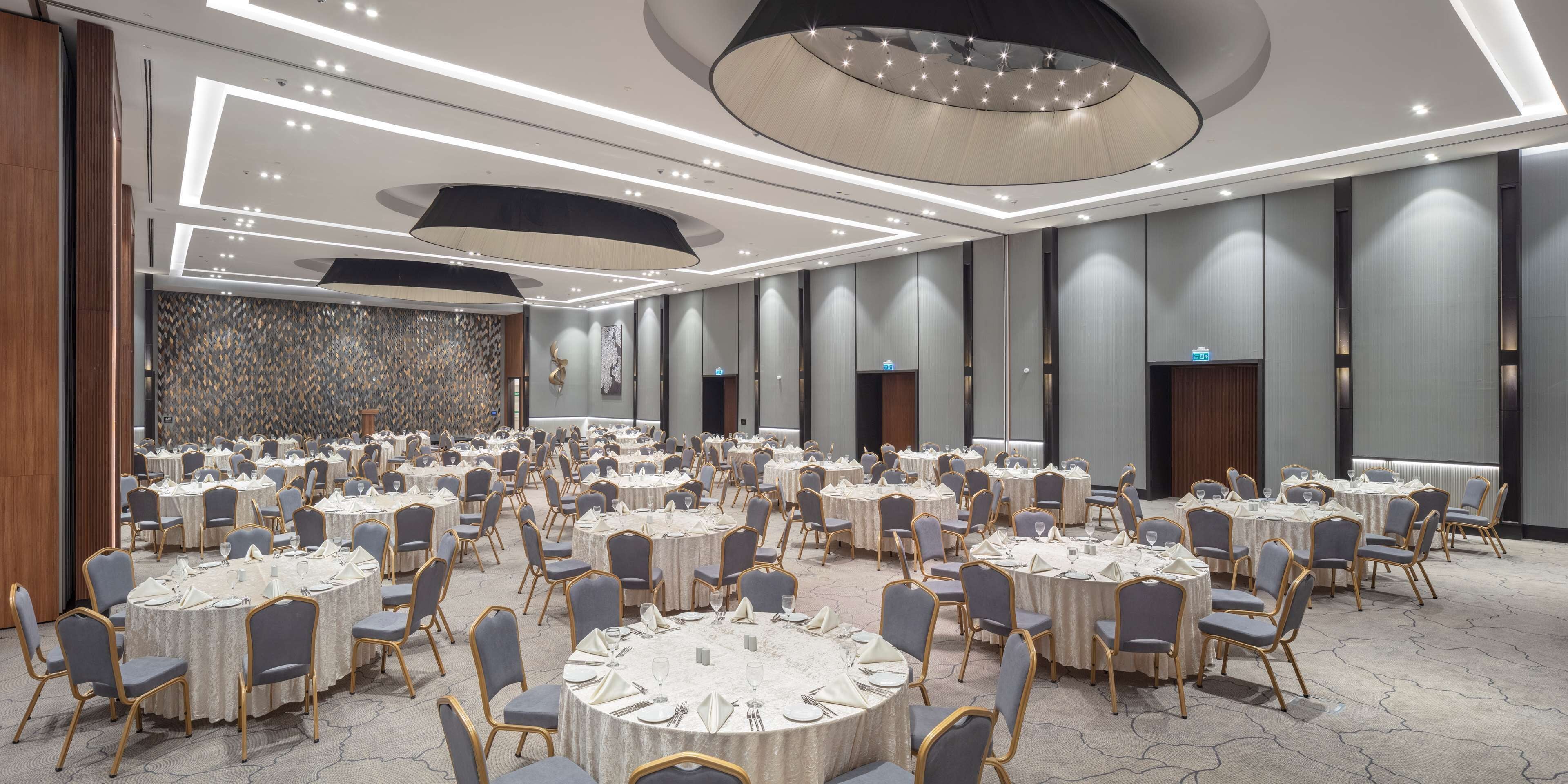 Un amplio salón de banquetes con mesas y sillas redondas, iluminación moderna y un papel tapiz estampado.