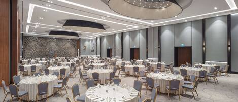 Un amplio salón de banquetes con mesas y sillas redondas, iluminación moderna y un papel tapiz estampado.