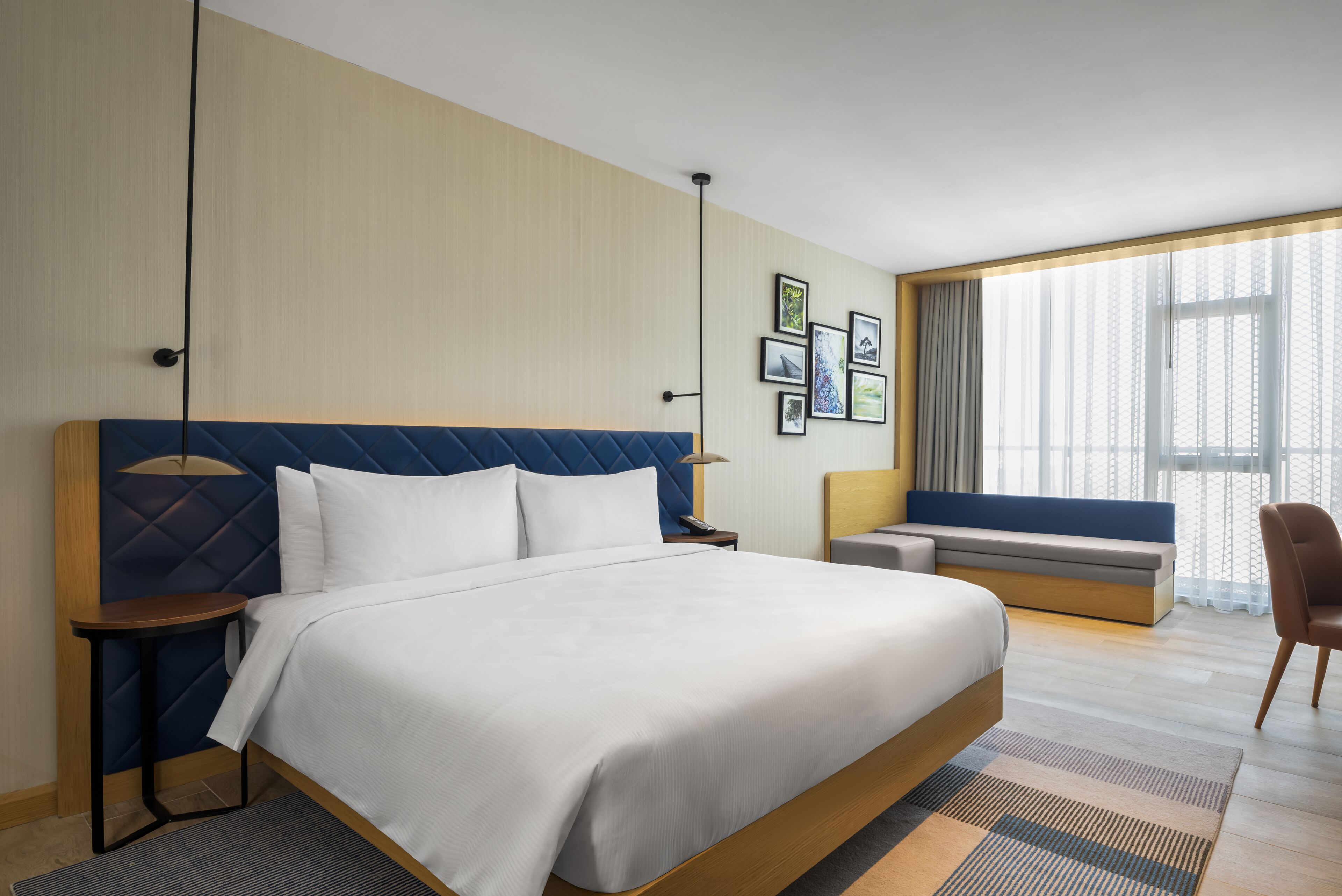 A hotel room with a large bed, a bedside table, a chair, a sofa, and a window with curtains.