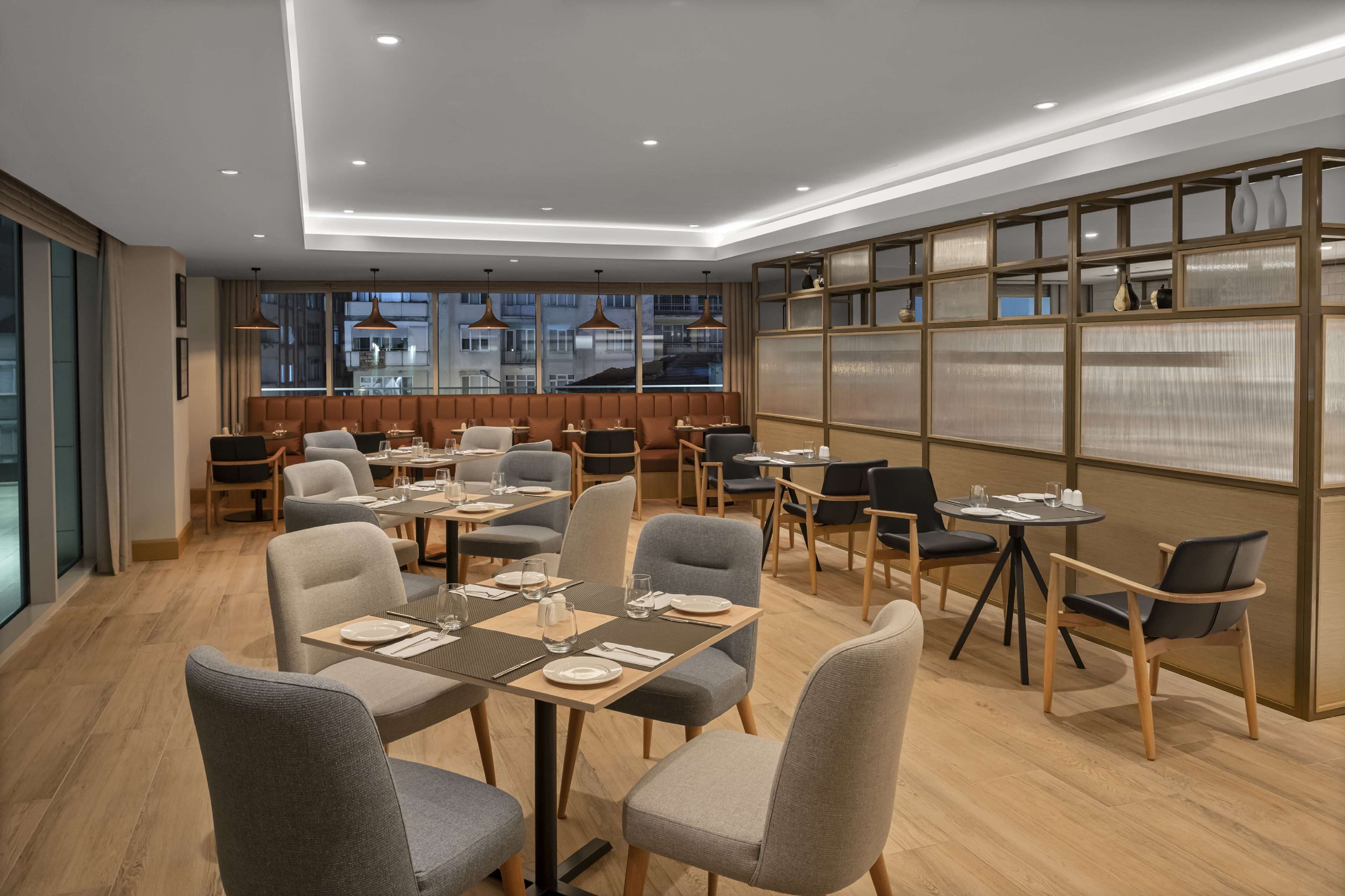 A modern dining area with tables and chairs, large windows, and a decorative wall with shelves.