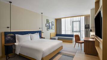 A hotel room with a large bed, a desk, a chair, a TV, and a window with curtains.