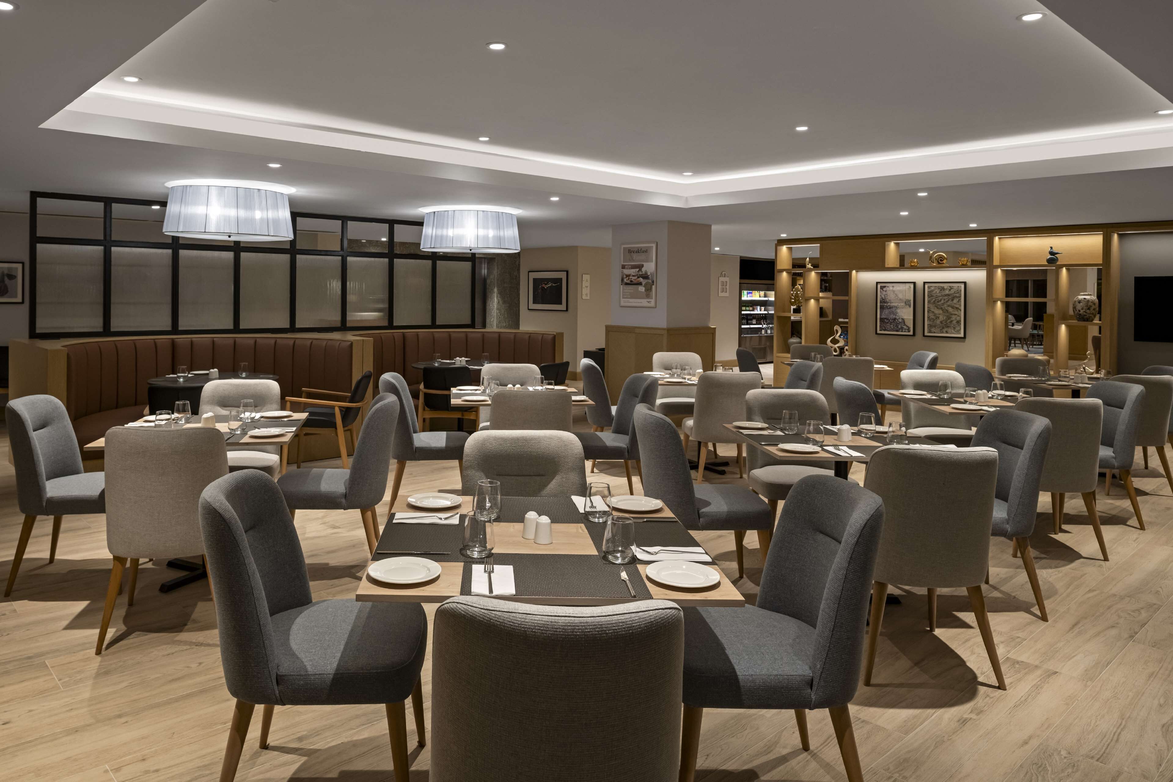 Un'area pranzo moderna con diversi tavoli e sedie, illuminazione soffusa e un design d'interni contemporaneo.