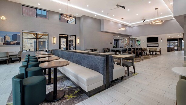 A modern hotel lobby with a long bench seating area, multiple tables, and contemporary lighting fixtures. - Homewood Suites by Hilton Oklahoma City Quail Springs (Oklahoma City)