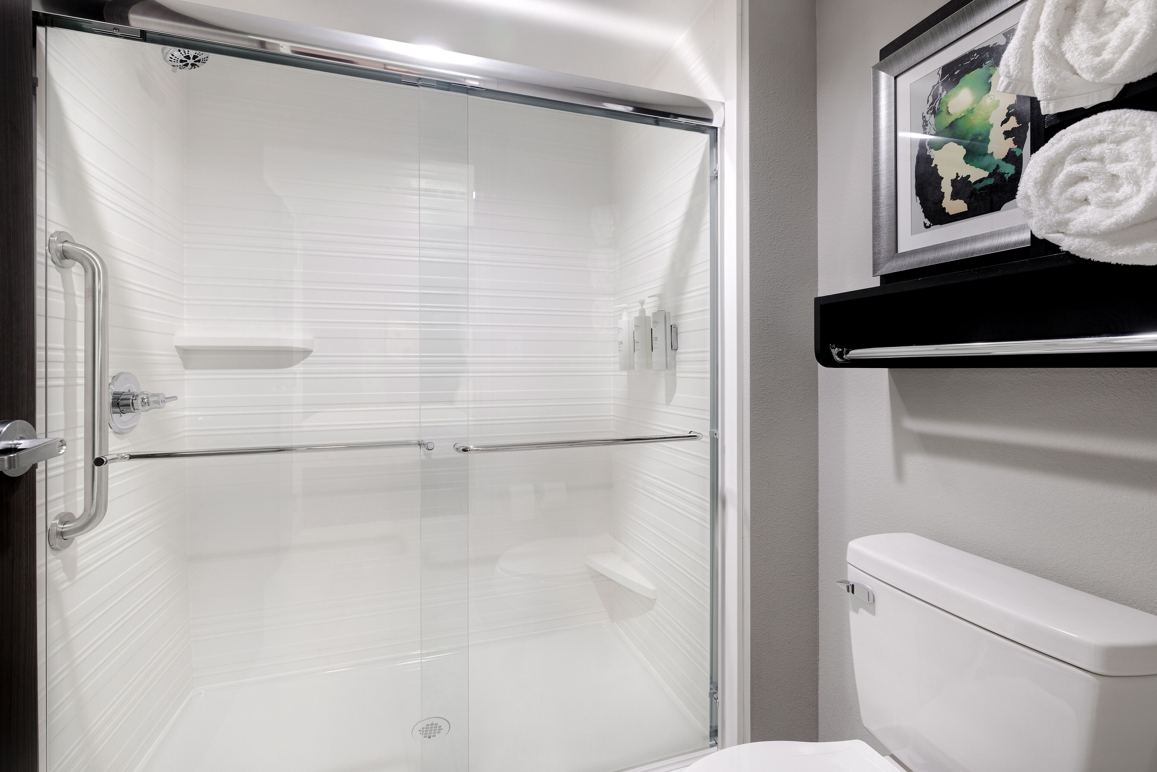 A modern bathroom with a glass-enclosed shower, a white toilet, and a shelf with towels.