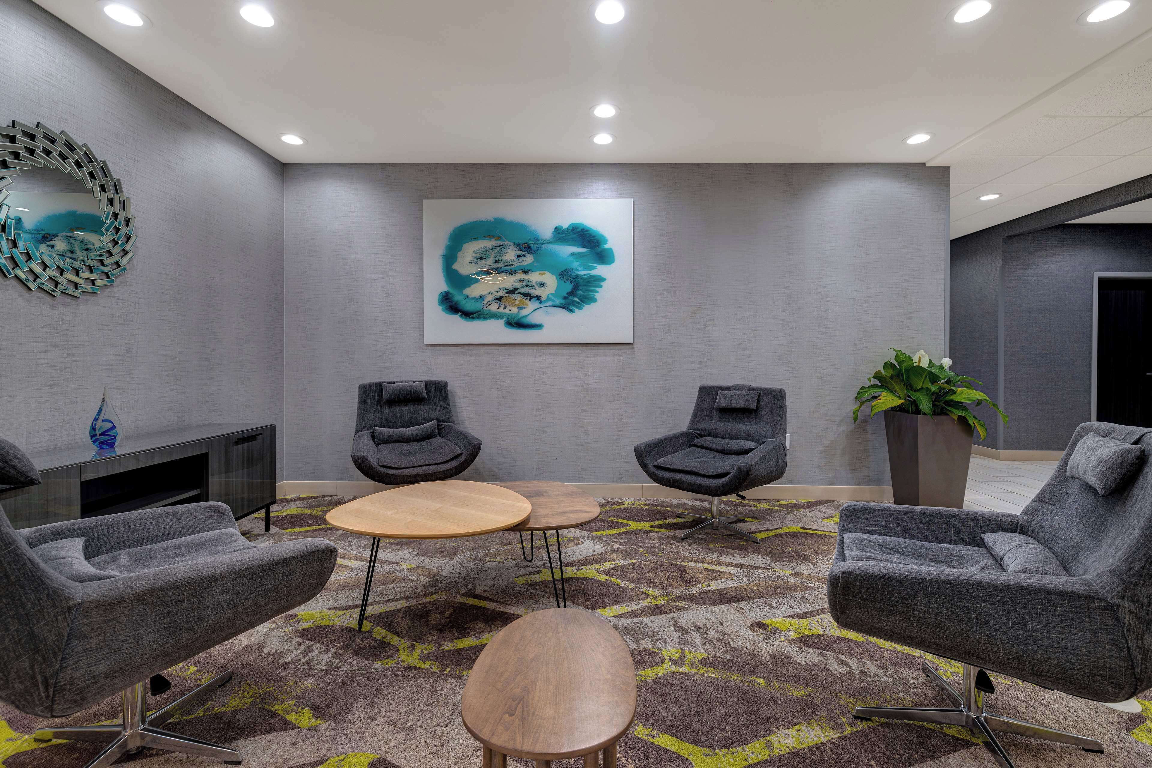 A modern lounge area with grey upholstered chairs, a wooden coffee table, and a large abstract painting on the wall.