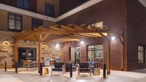 An outdoor patio area with wooden furniture, a grill, and a stone wall. - Homewood Suites by Hilton Oklahoma City Quail Springs (Oklahoma City)