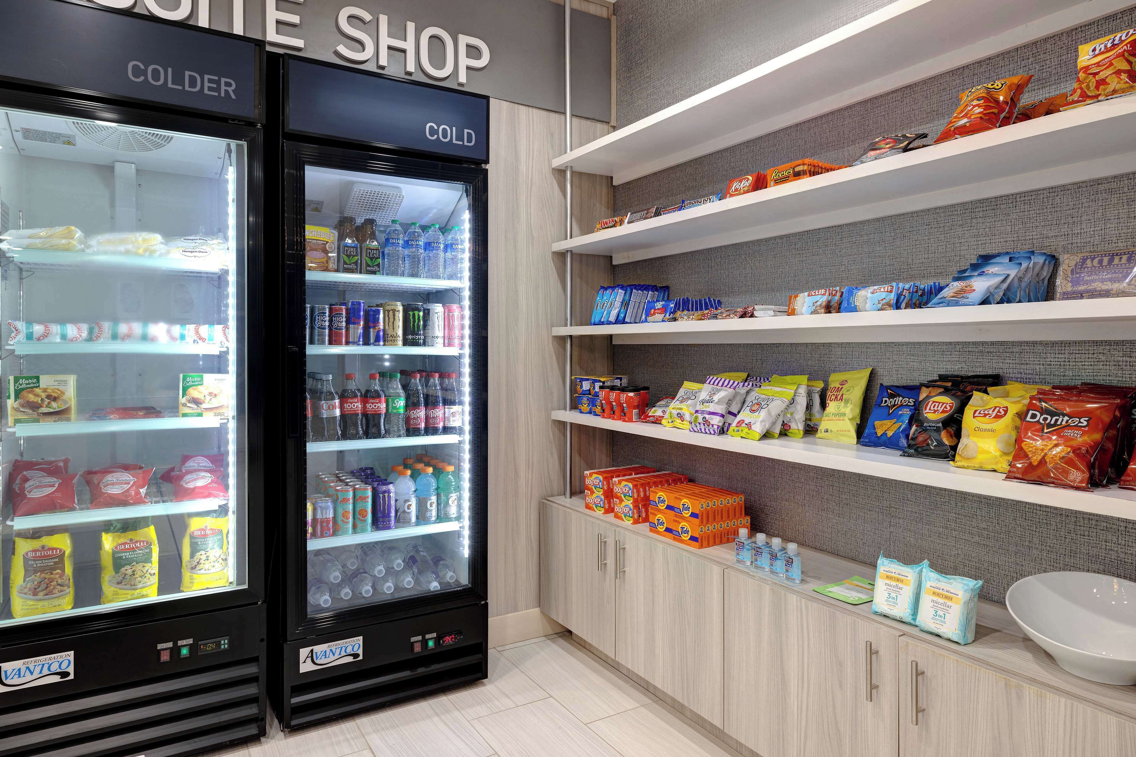 Zona de máquinas expendedoras con una sección 'COLDER' y un estante repleto de aperitivos y bebidas.