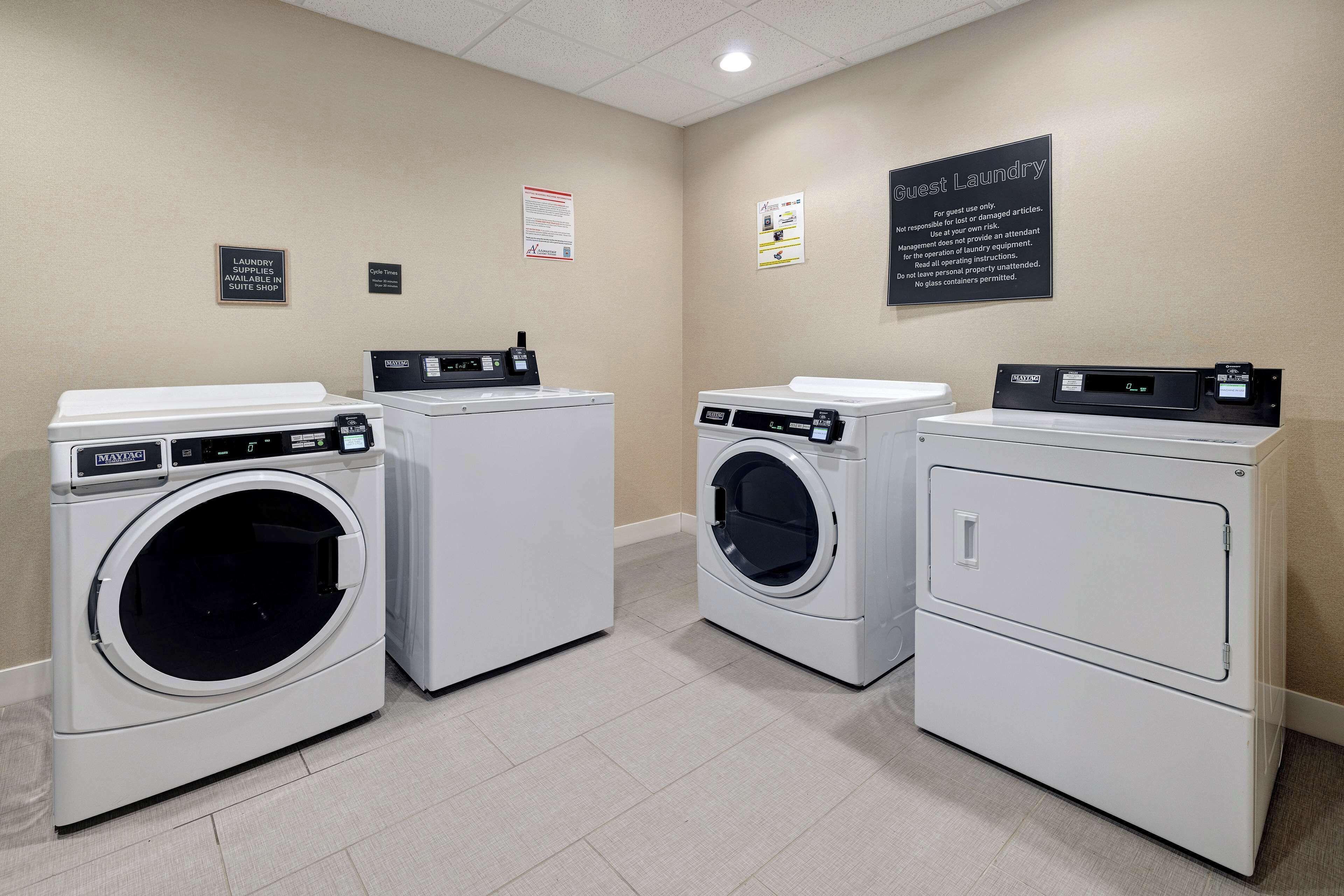 A laundry facility with three washing machines and a sign indicating guest laundry services.