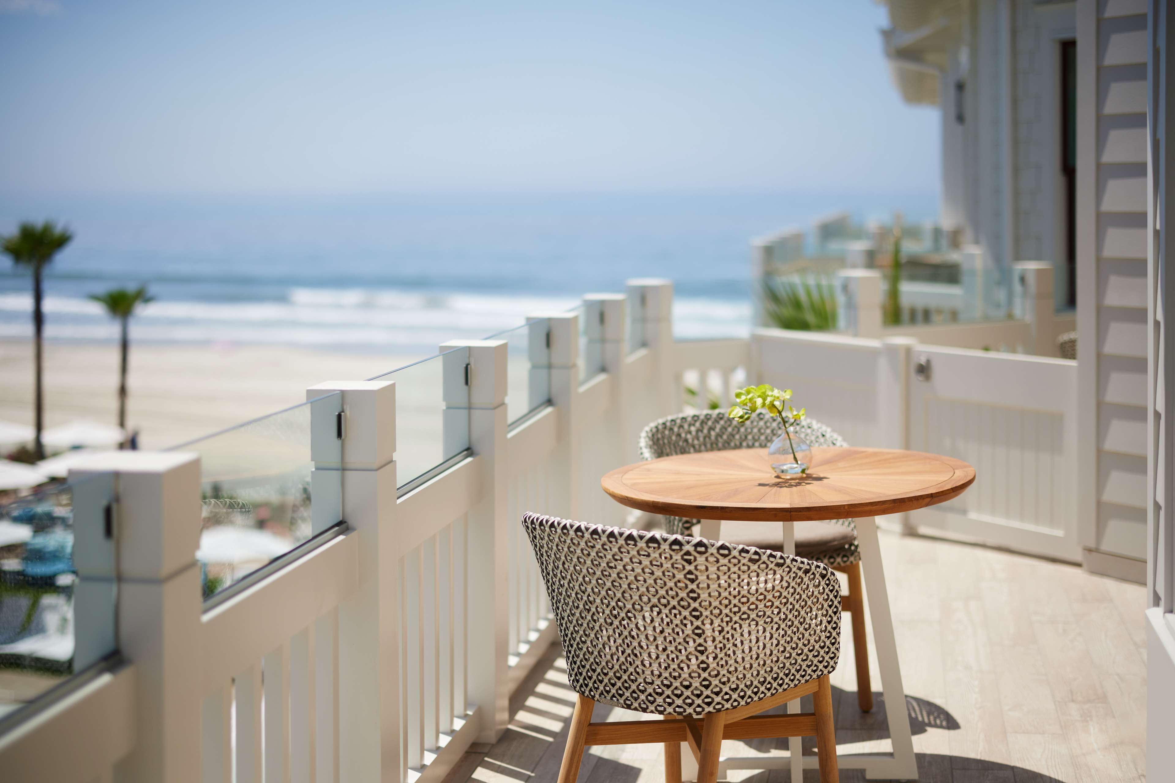 A balcony with a view of the beach, a round wooden table, and two patterned chairs.
