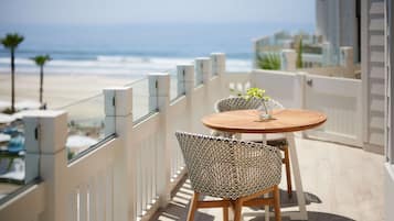 A balcony with a view of the beach, a round wooden table, and two patterned chairs.