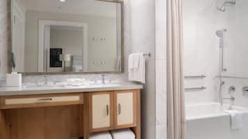 A modern bathroom with a large mirror, two sinks, wooden cabinets, and a bathtub.