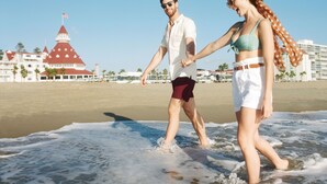 A couple walking on a beach with a large building in the background. - Shore House at The Del, LXR Hotels & Resorts (Coronado)
