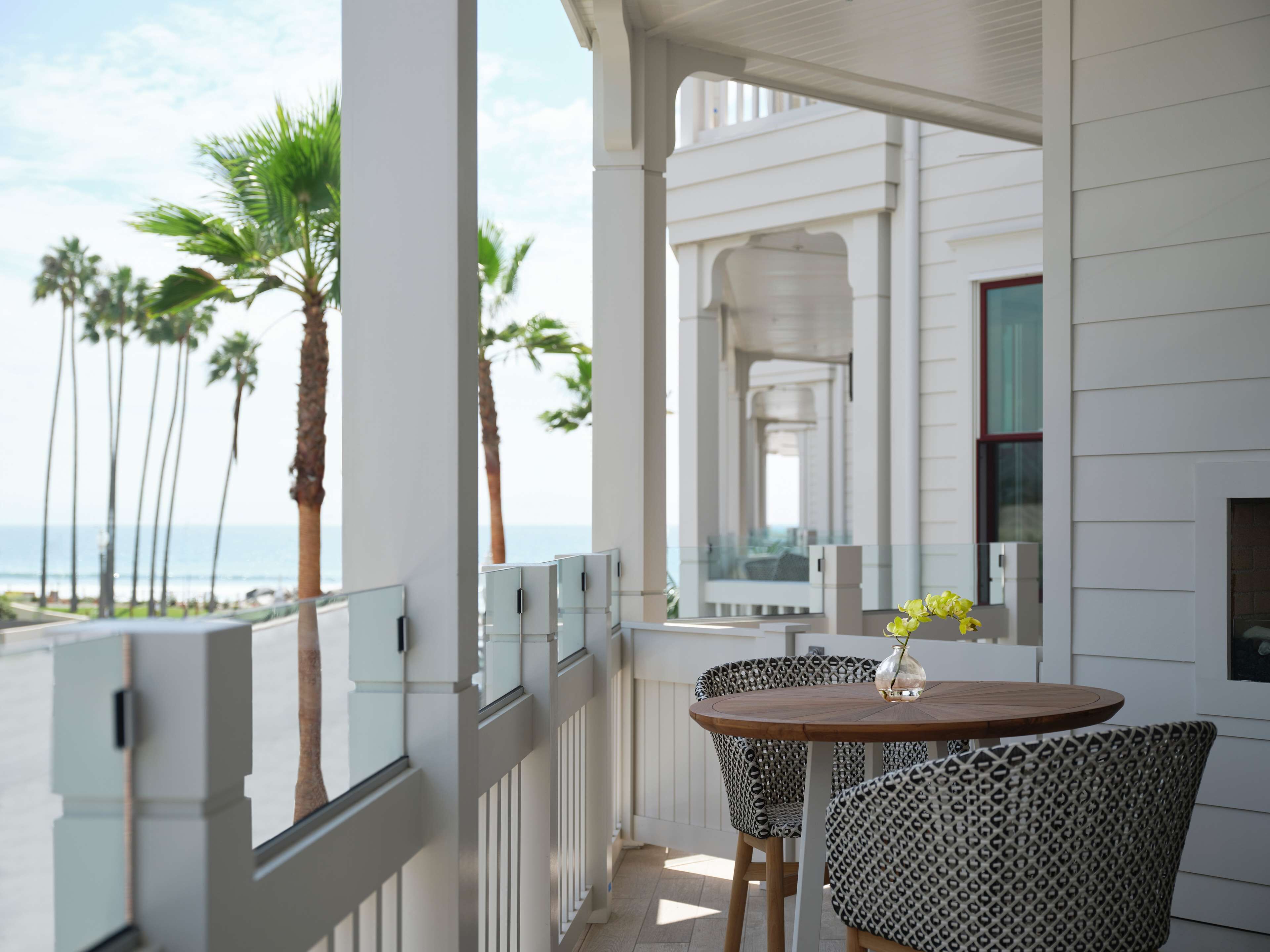 A balcony with a view of the ocean, featuring a table and chairs, and a vase with flowers.