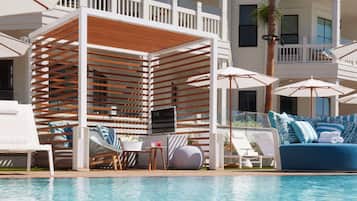 A poolside area with lounge chairs, umbrellas, a wooden pergola, and a blue sofa with pillows.