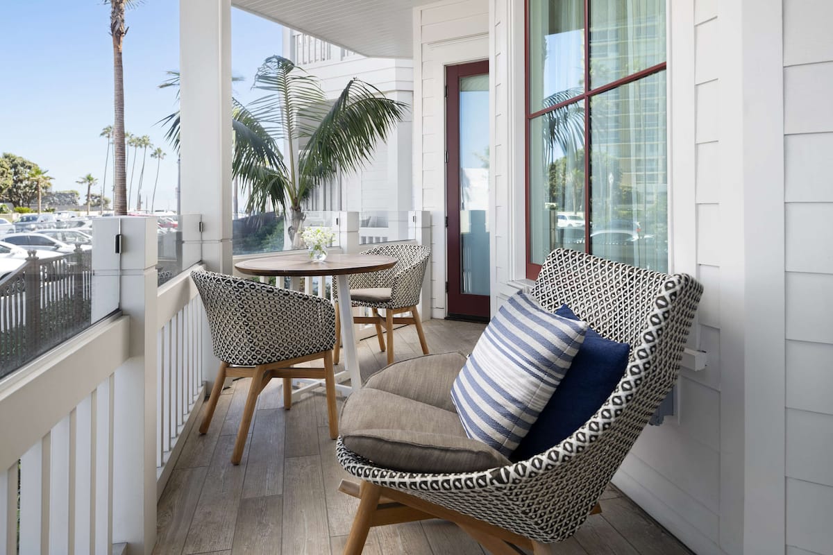 A balcony with a table and two patterned chairs, overlooking a parking area and palm trees.