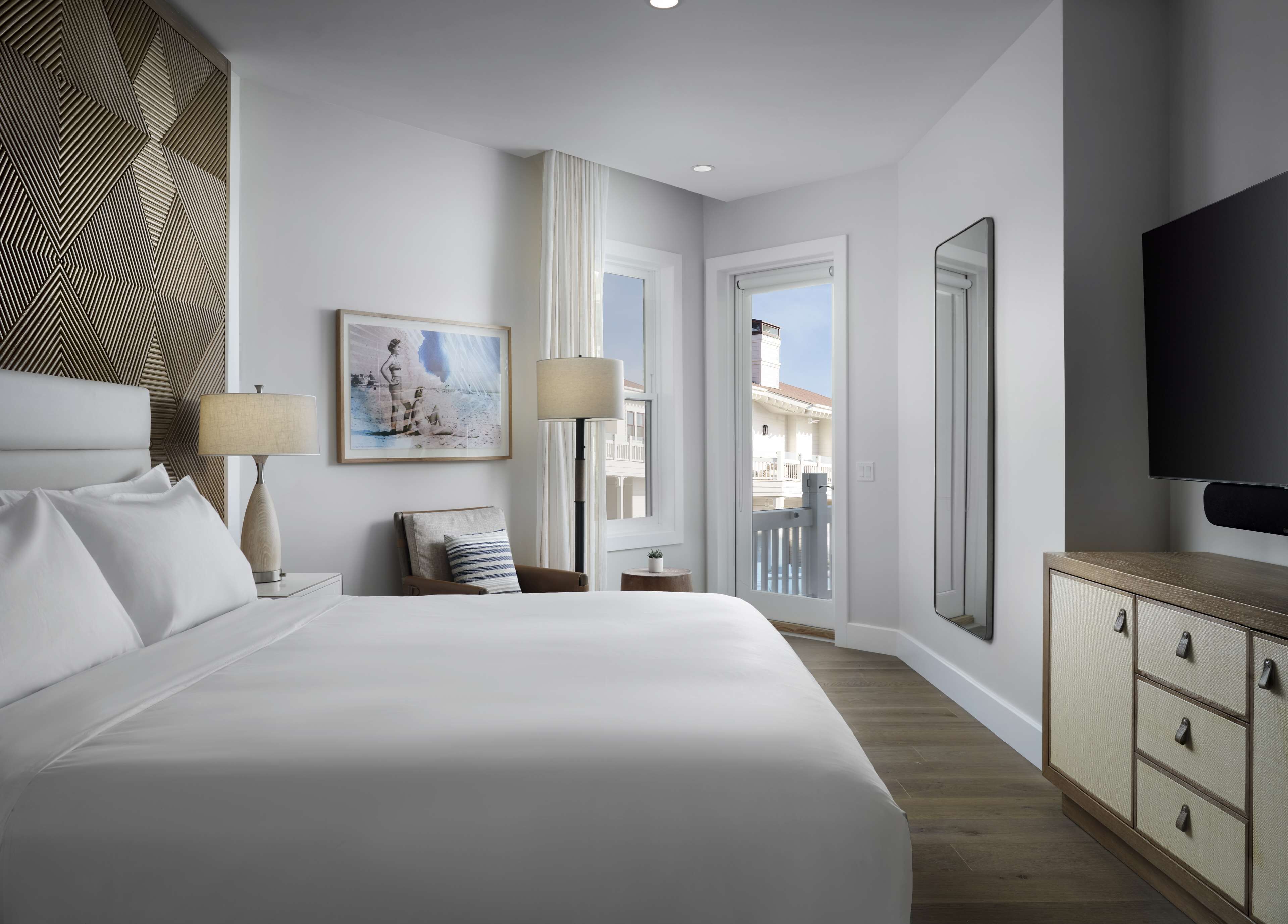 A modern hotel room with a large bed, two bedside tables, a TV, a balcony, and a patterned wall.