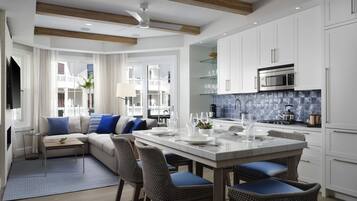 Una cucina moderna con mobili bianchi, un'isola centrale con sgabelli da bar e un'area pranzo con divano e cuscini blu.
