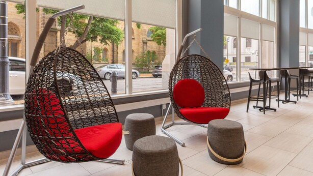 A modern interior with hanging chairs and ottomans, large windows with a view of the street. - Home2 Suites by Hilton St. Louis Downtown (St. Louis)