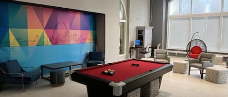 A modern indoor pool table with a colorful mural, comfortable seating, and a large window providing natural light.