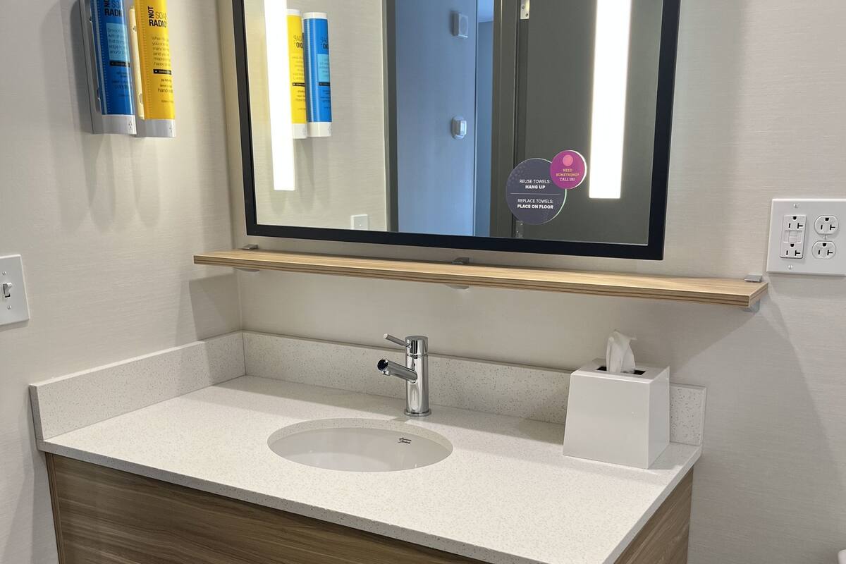 A modern bathroom with a large mirror, a sink, and a towel rack.