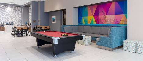 A pool table in a modern lounge area with a colorful geometric wall art and a seating area.