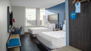 Camera d'albergo con due letti, una scrivania, una sedia, una televisione e un'ampia finestra con vista sulla città.