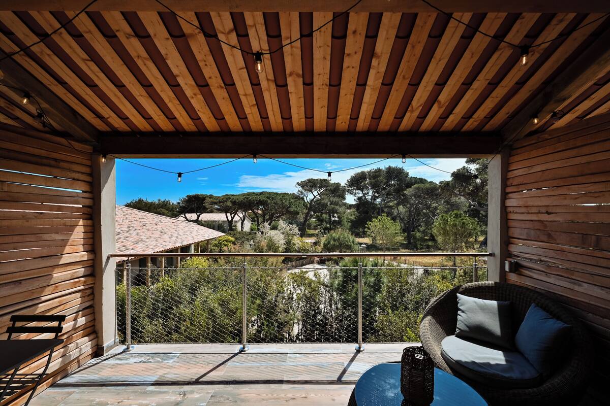 A wooden ceiling, a wicker chair, a table, a view of trees and a fence.