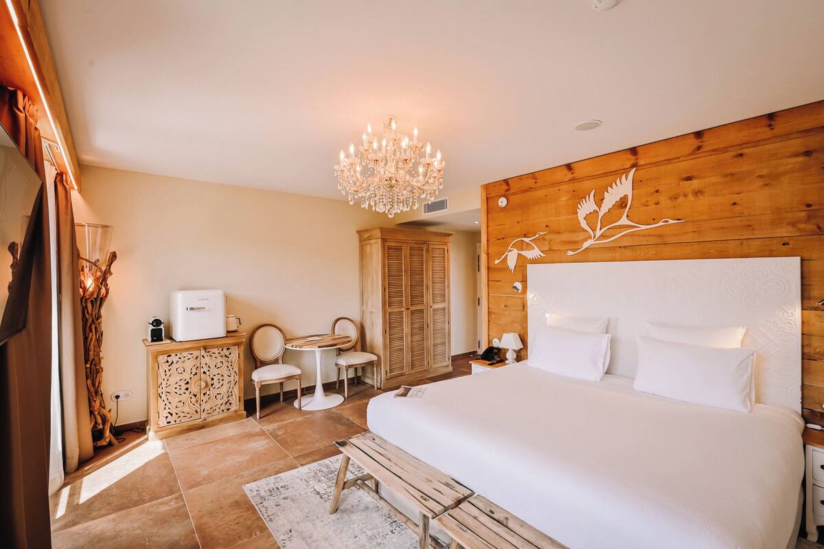 A bedroom with a large bed, a wooden headboard, a chandelier, a small table, and a cabinet.