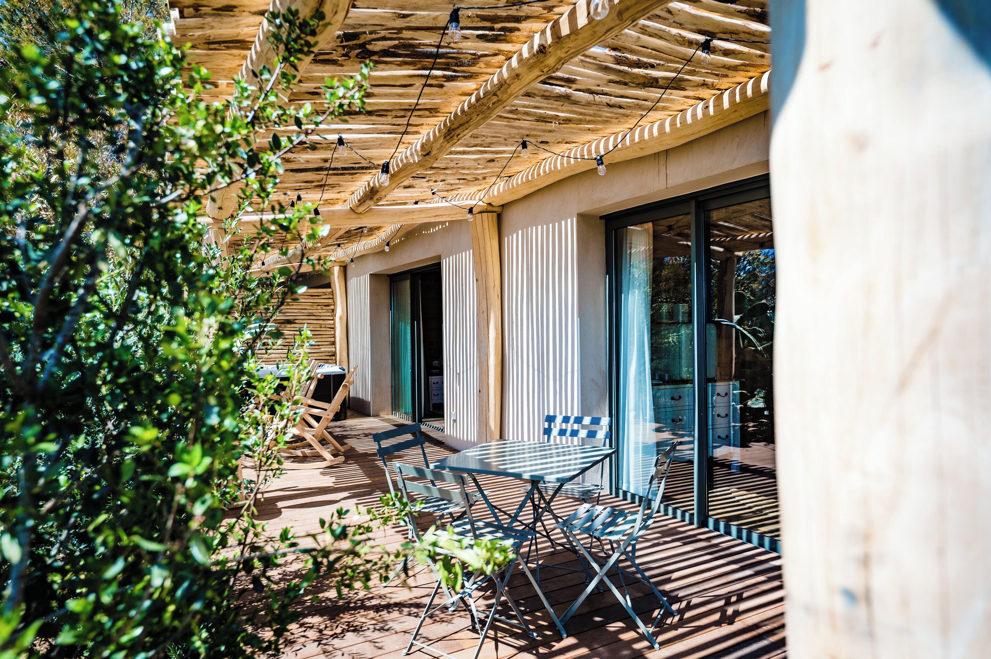 A wooden deck with outdoor furniture, a pergola, and a glass door leading to a room.
