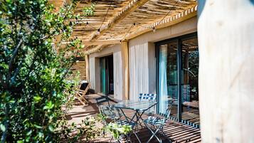 A wooden deck with outdoor furniture, a pergola, and a glass door leading to a room.