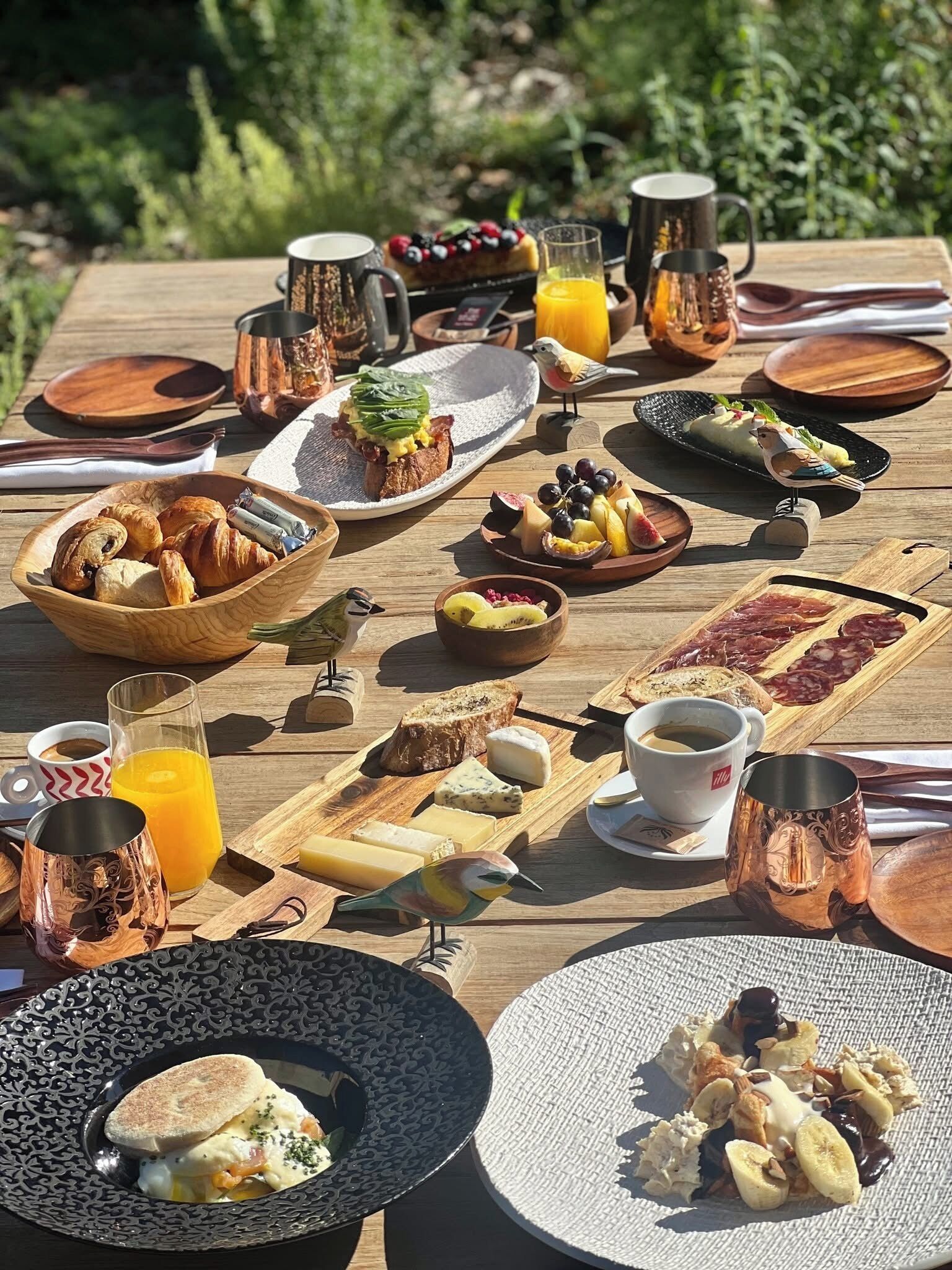 Een ontbijt op een houten tafel met diverse etenswaren, drankjes en decoratieve vogels.