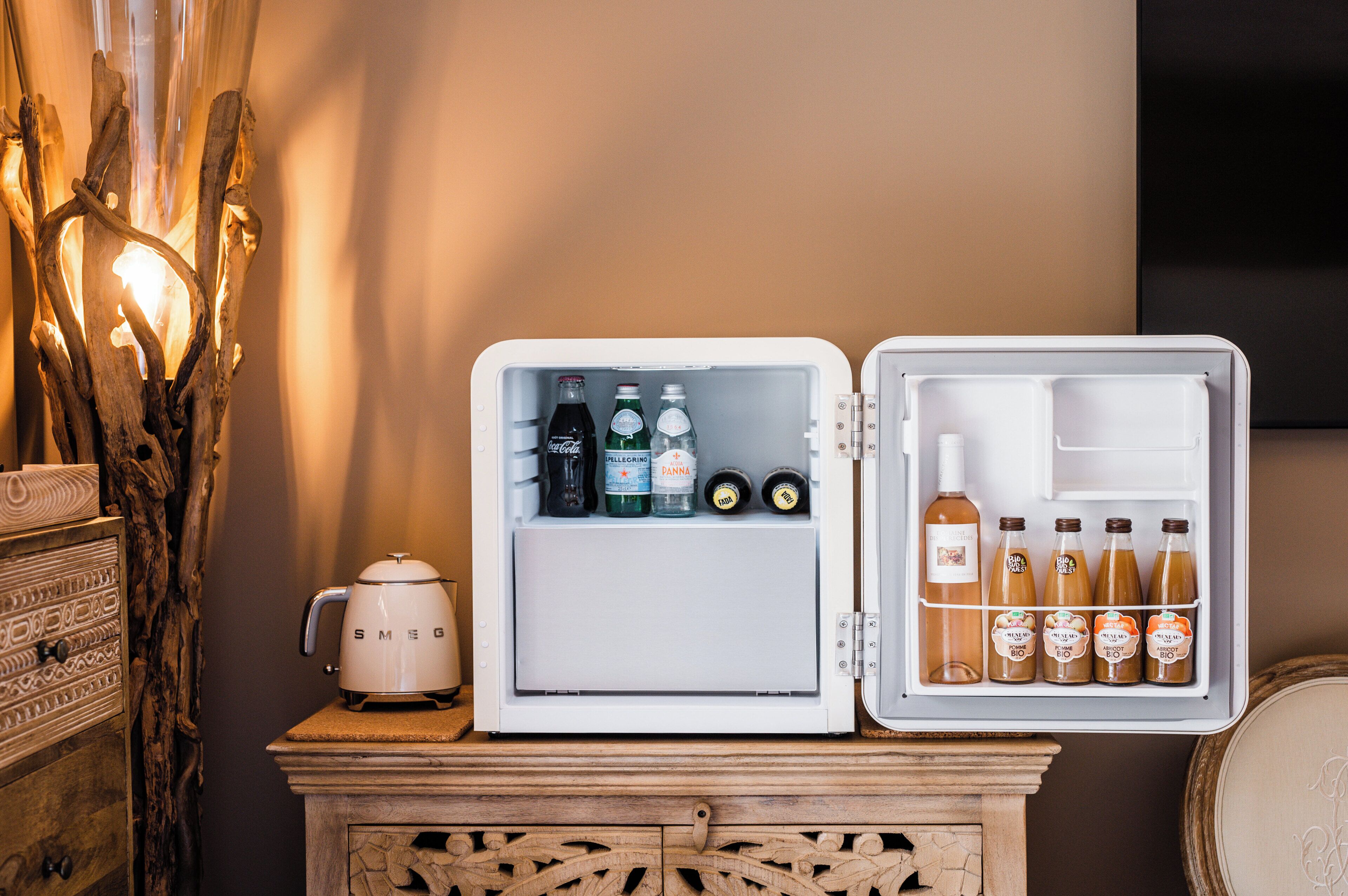 Geladeira aberta com bebidas e uma cafeteira em um armário de madeira.