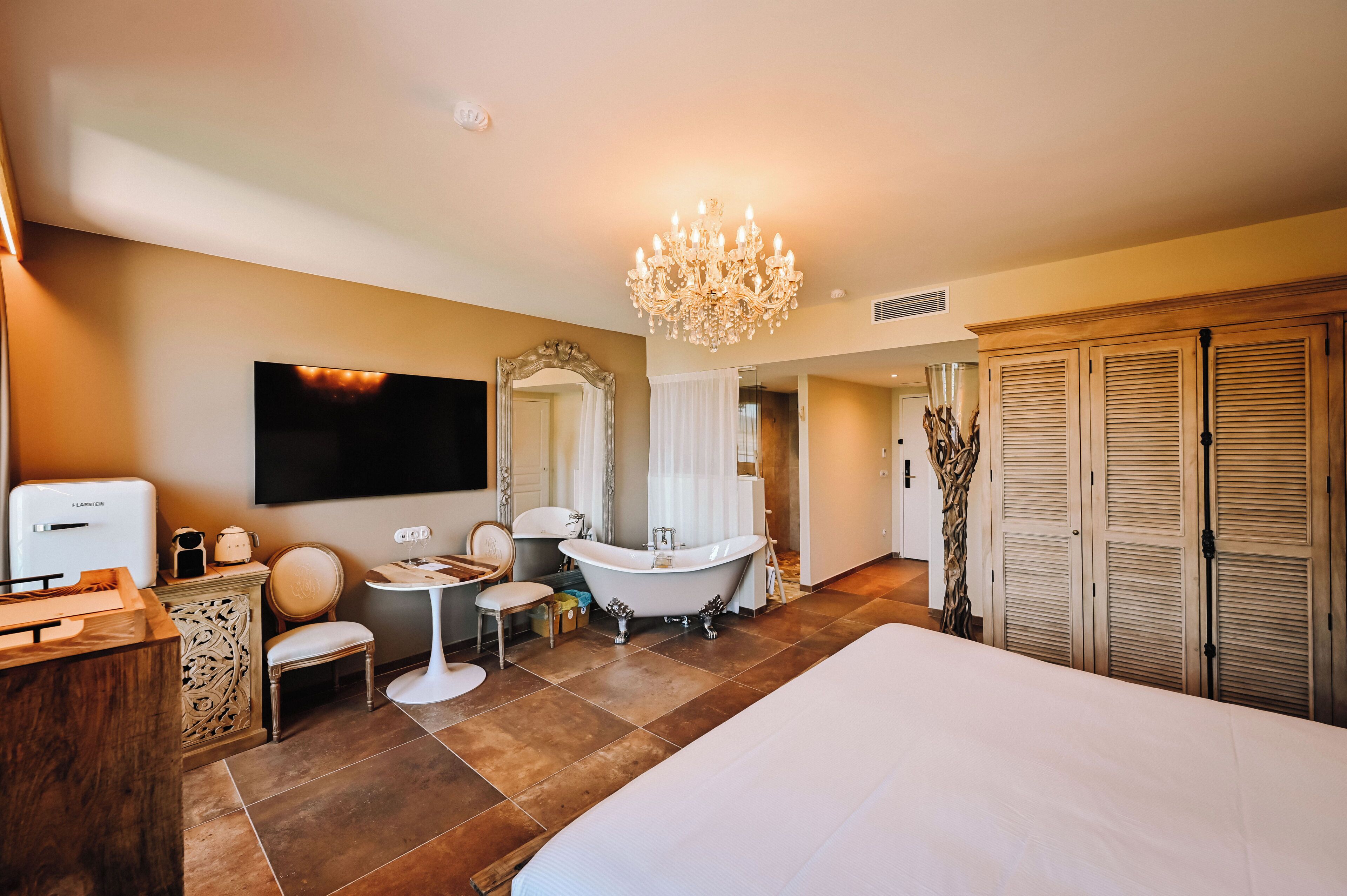 Une chambre d’hôtel moderne dotée d’un grand lit, d’une baignoire, d’une coiffeuse avec un miroir, d’un lustre et d’une télévision.