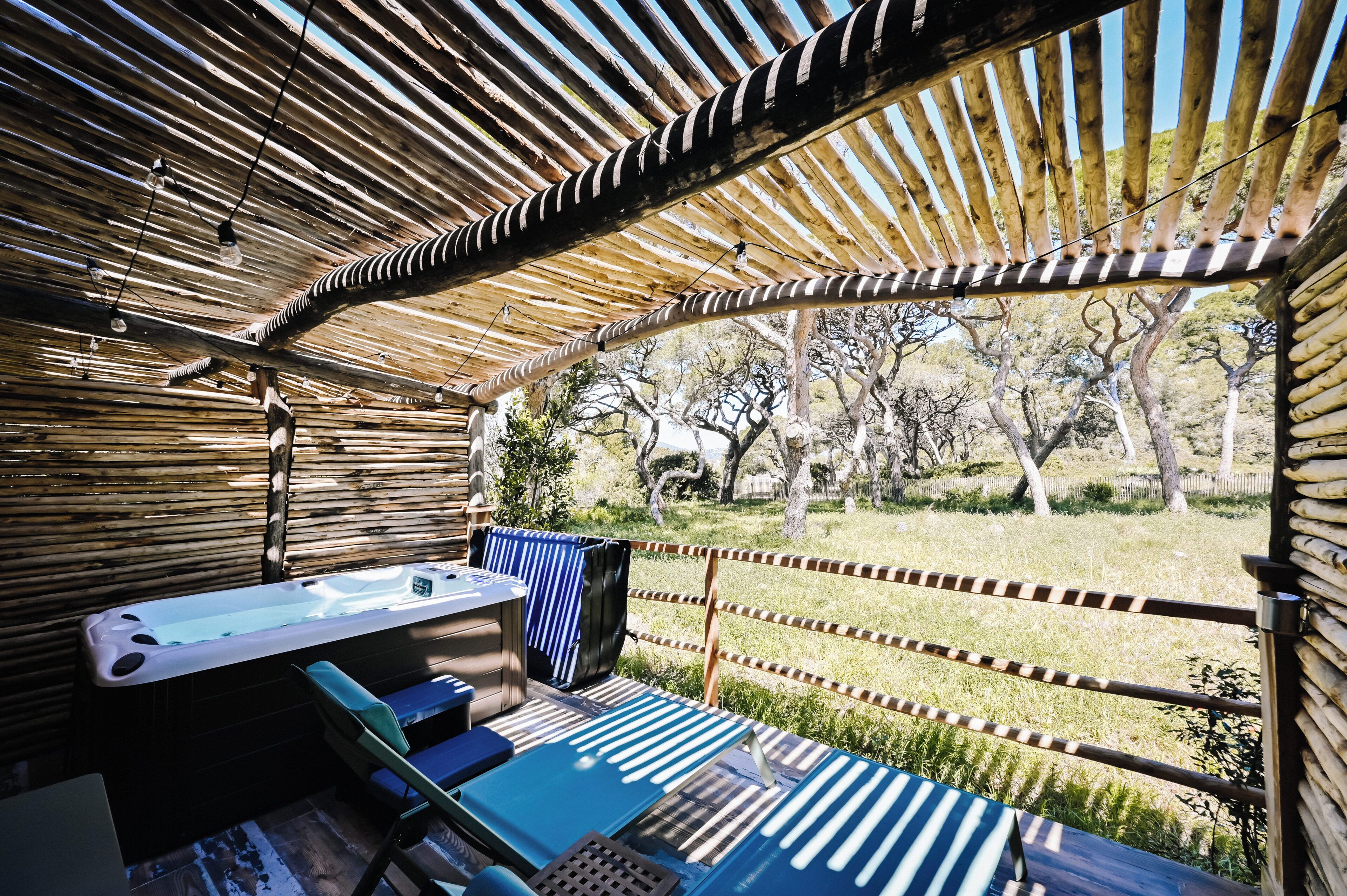 A covered outdoor area with a hot tub, seating, and a view of trees.