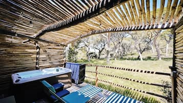 A covered outdoor area with a hot tub, seating, and a view of trees.