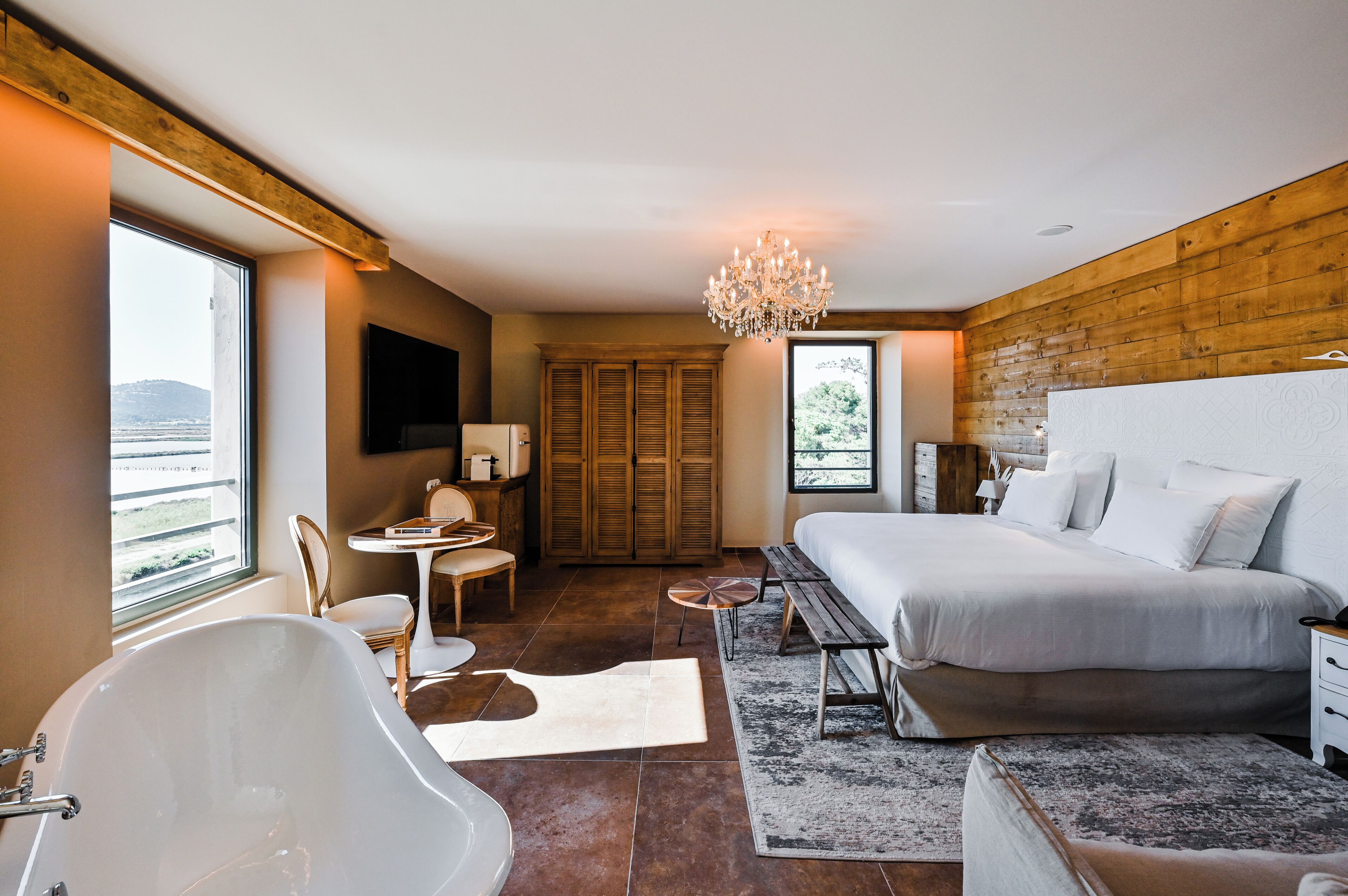Un dormitorio con una cama grande, una bañera, un escritorio y vistas al exterior.