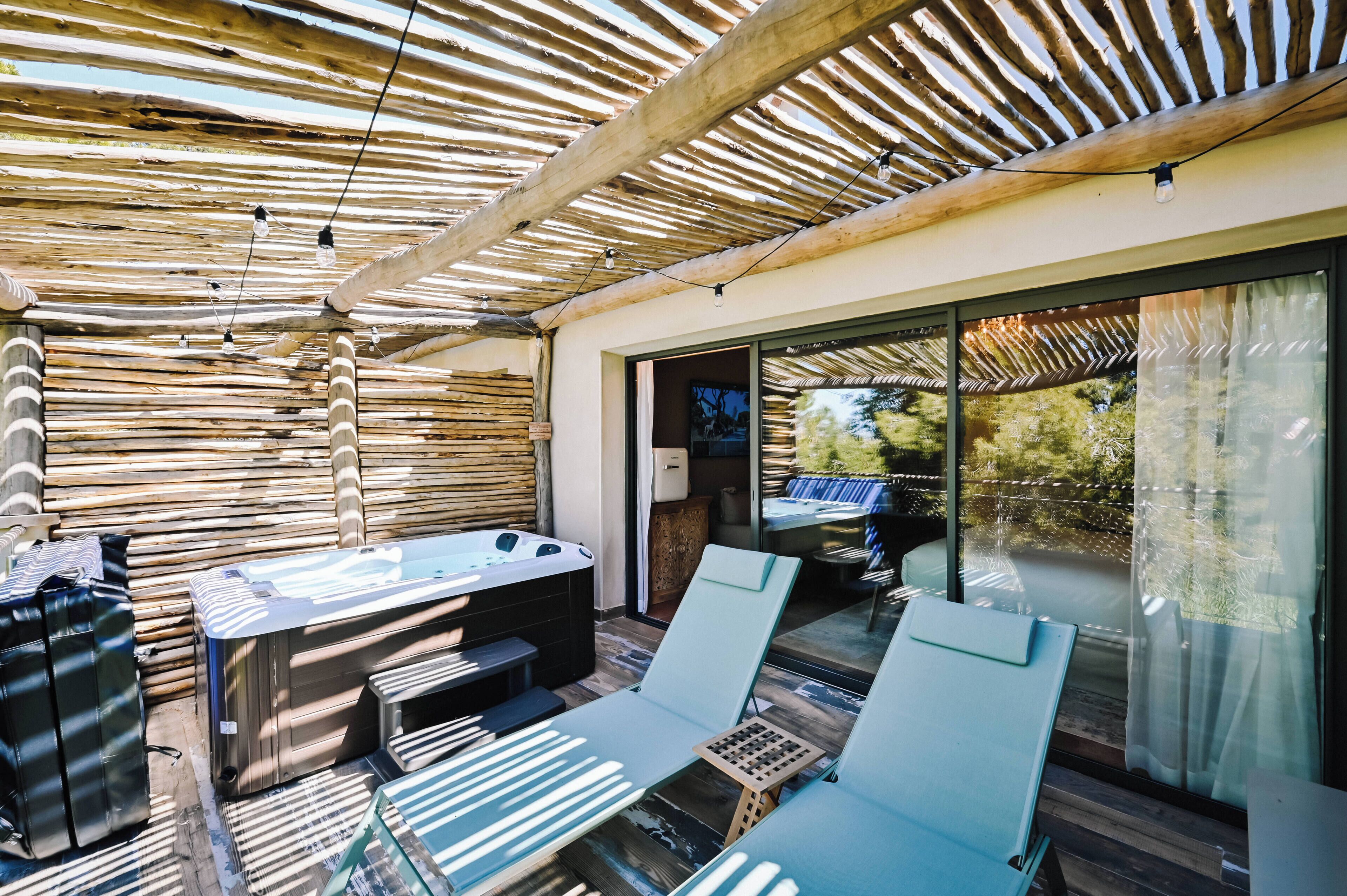 Un patio exterior con un jacuzzi, sillones de descanso y una pérgola de madera.