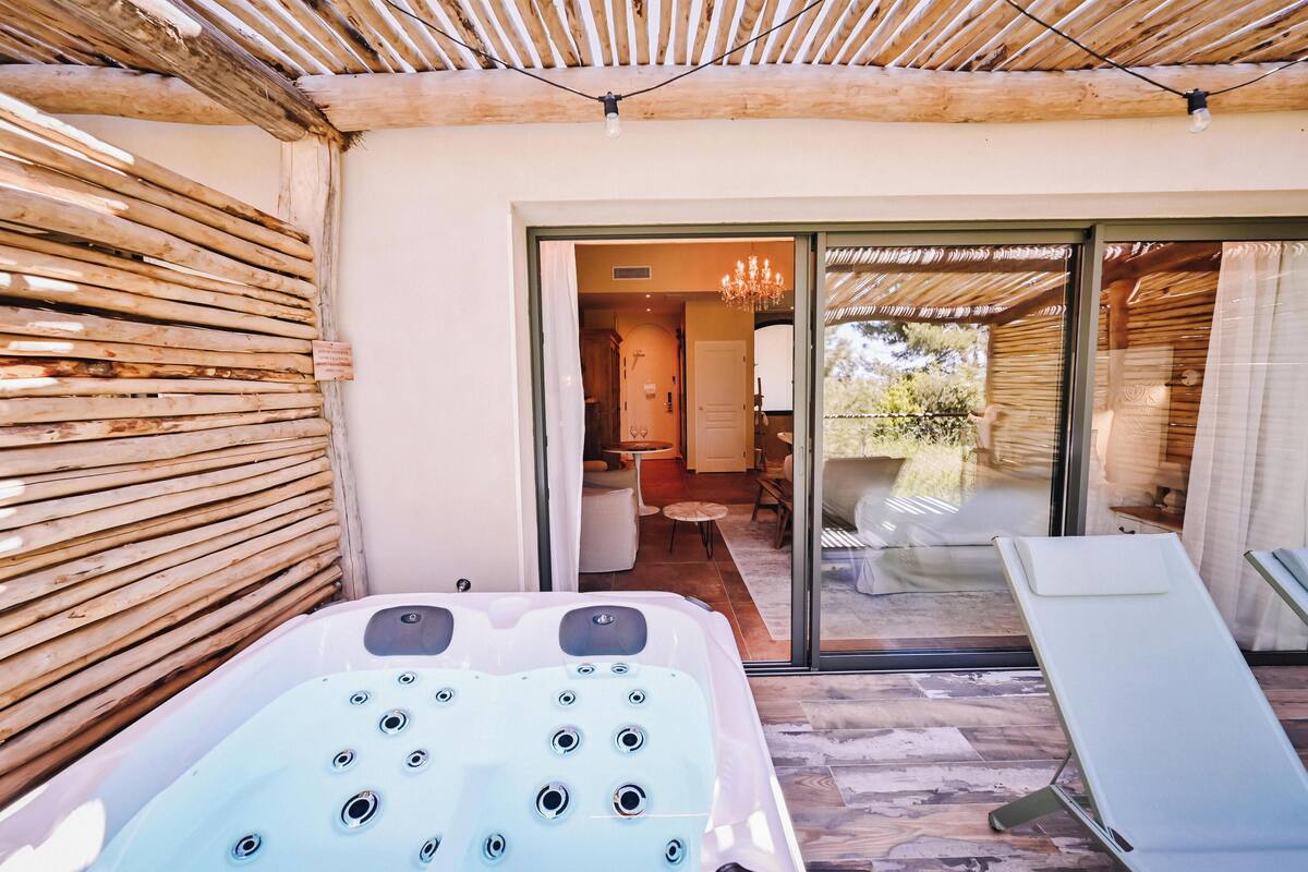 A spa area with a hot tub, a lounge chair, and a glass door leading to a room with a chandelier.