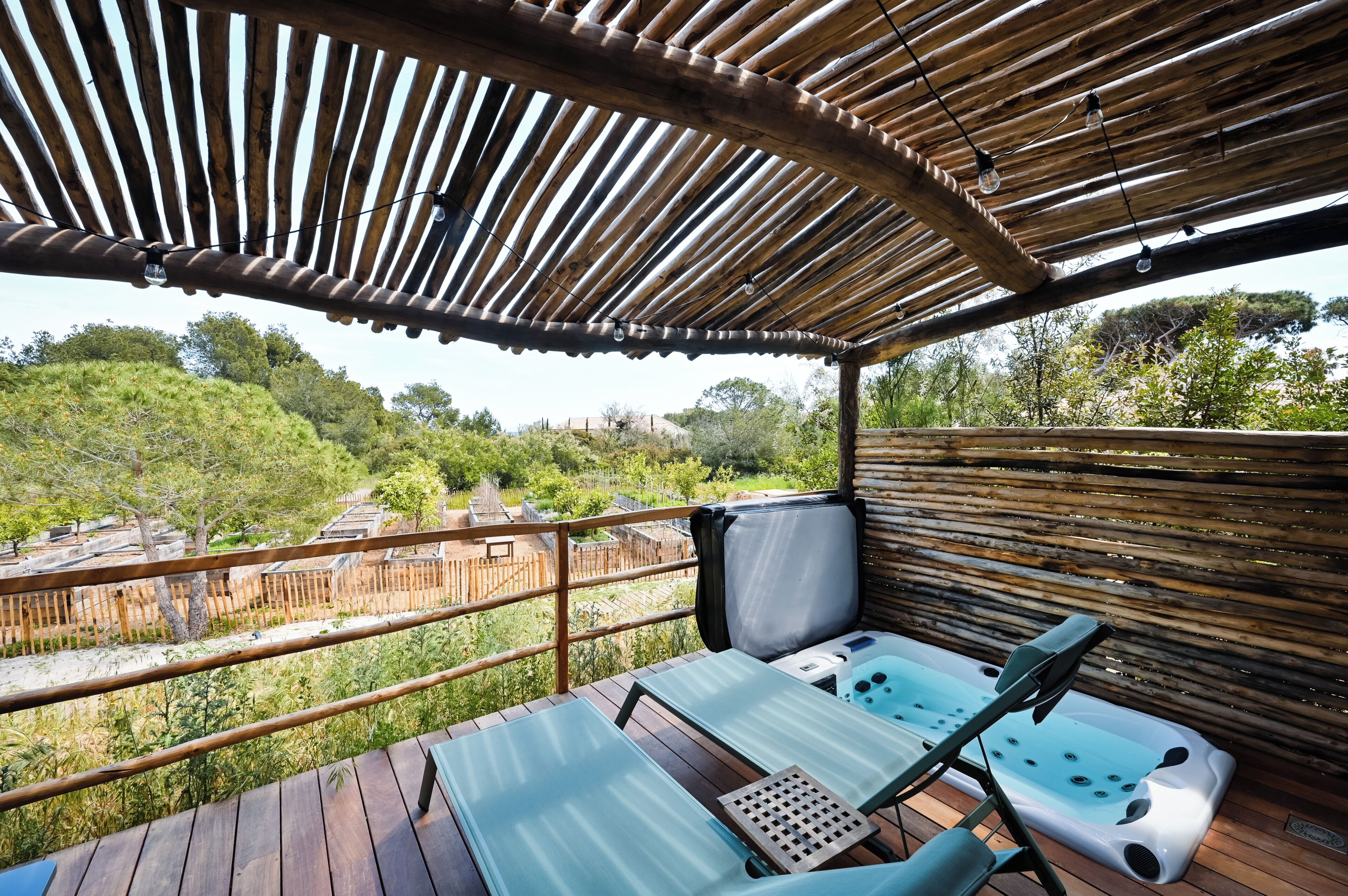 Una terraza de madera con zona de estar cubierta, un jacuzzi y vistas a un paisaje natural.