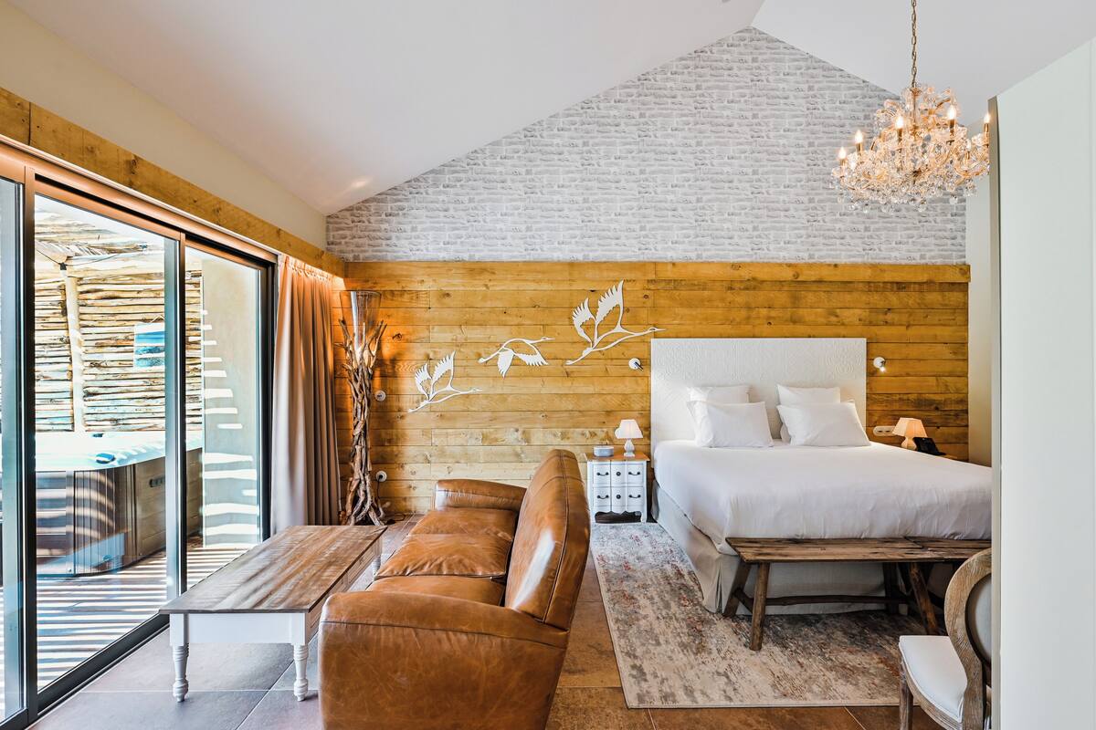 A bedroom with a large bed, a wooden headboard, a chandelier, and a view through a glass door.