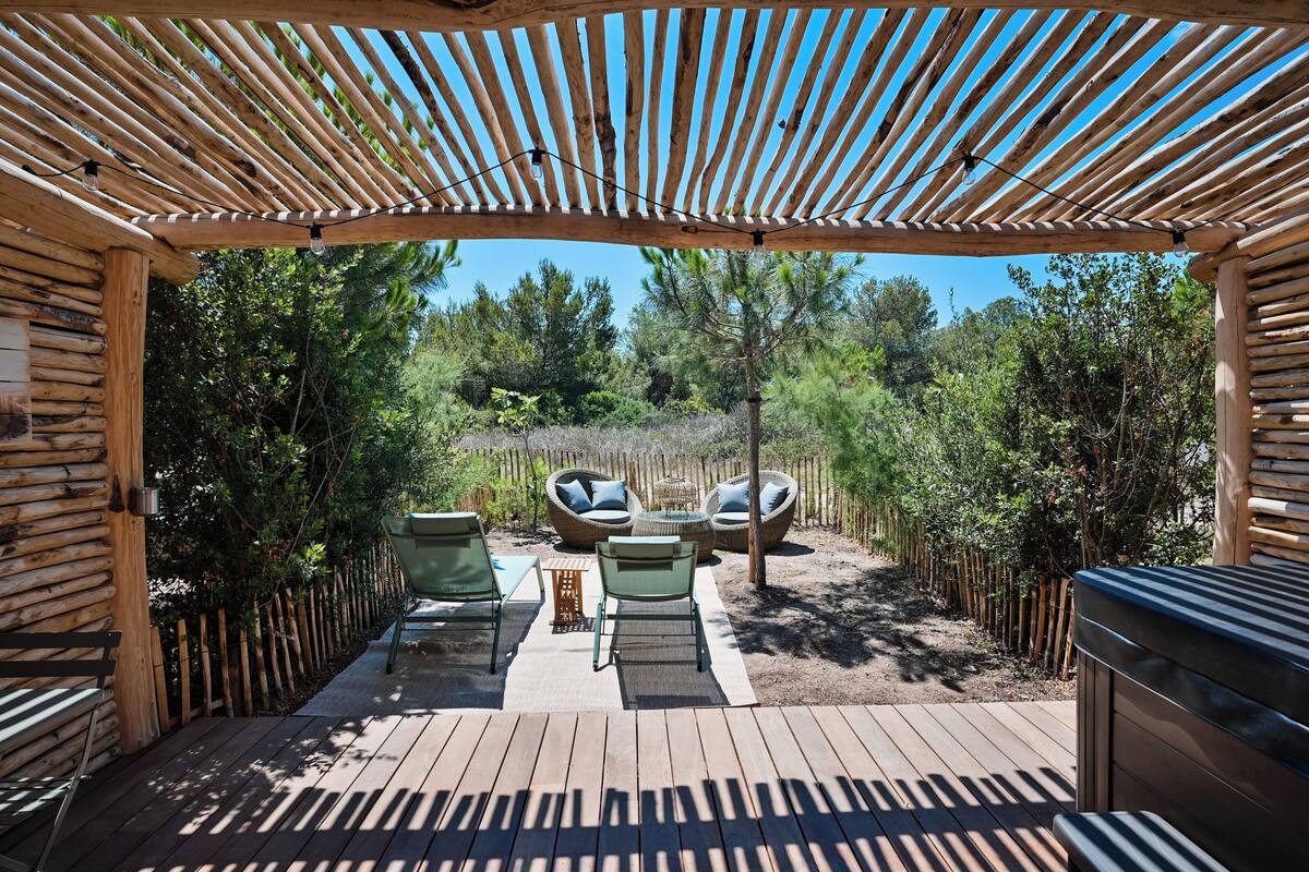A wooden deck with outdoor furniture, a pergola, and a view of a forested area.