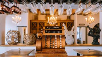 Une vieille caisse enregistreuse, accompagnée d’une liste de prix, entourée d’objets décoratifs et de verres suspendus.