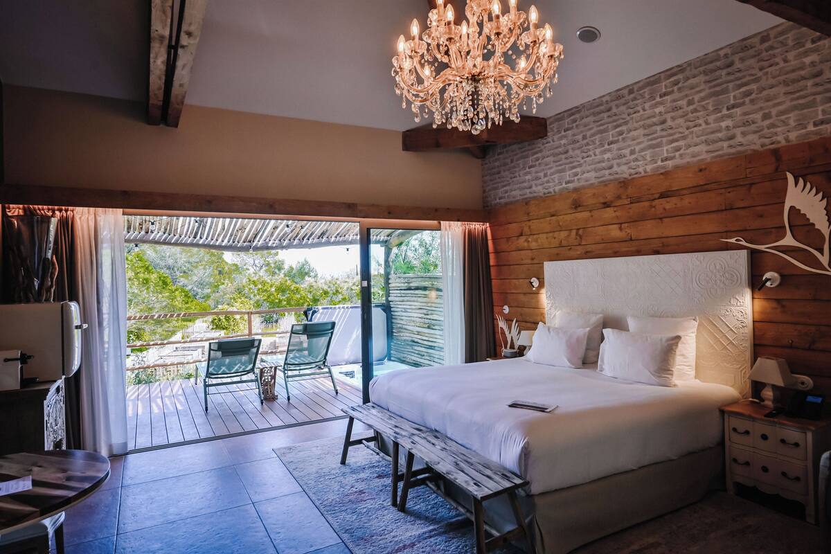 A bedroom with a large bed, a chandelier, a wooden headboard, and a balcony with a table and chairs.