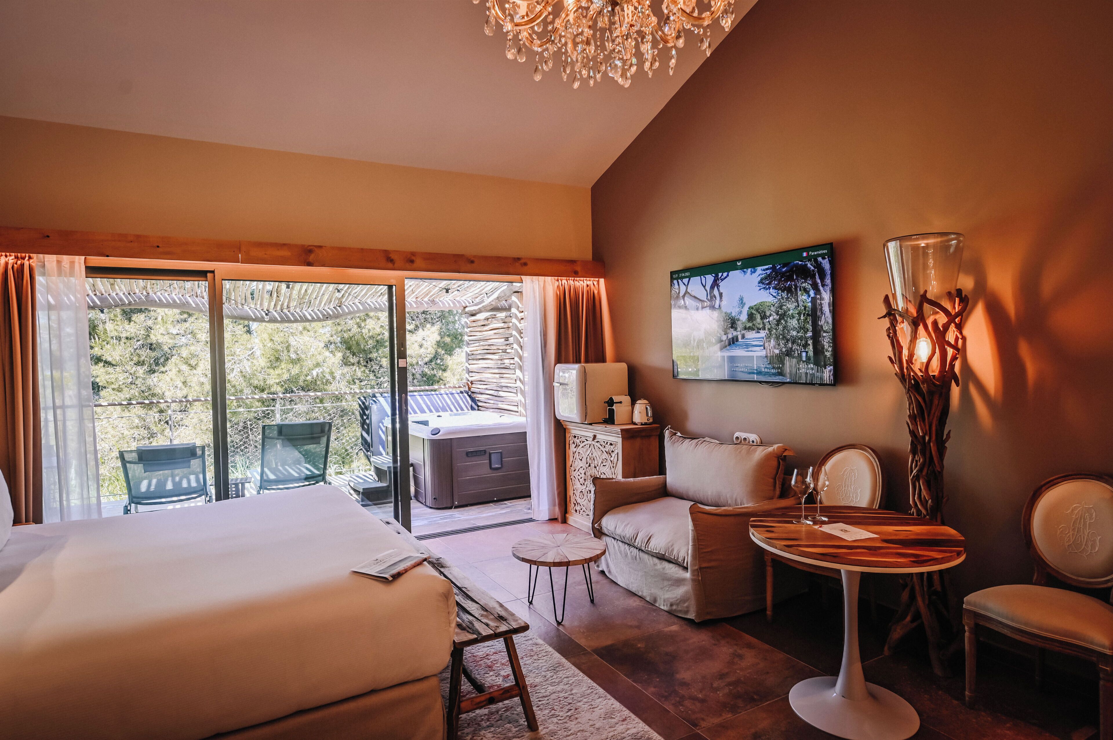 A hotel room with a bed, a sofa, a small table, a chair, a hot tub, and a large window with curtains.
