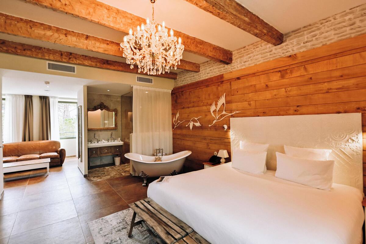 A bedroom with a large bed, a wooden wall, a chandelier, and a bathtub.